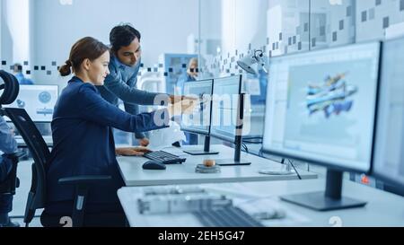 Inside Factory Office: Male Project Supervisor Talks to a Female Industrial Engineer who Works on Computer, Talk. In Workshop: Professional Workers Stock Photo