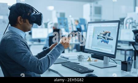 Modern Industrial Factory: Mechanical Engineer Wearing Virtual Reality Headset, Holding Controllers, Uses VR technology for Industrial Design Stock Photo