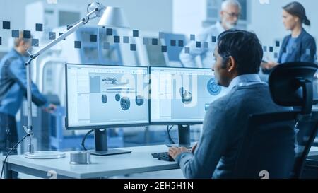 Modern Factory Office: Automotive Engineer Working on PC with Screen Showing 3D Car Concept Made in CAD. Workshop: Workers Use High-Tech Industrial Stock Photo