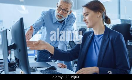 Modern Factory Office: Project Manager Supervisor Talk to a Female Engineer Working on Computer. Team of Professionals Solving Heavy Industry Problems Stock Photo