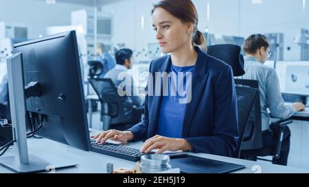Modern Factory Office: Portrait of Young and Confident Female Industrial Engineer Working on Computer. Industrial Factory with Industry Design Stock Photo
