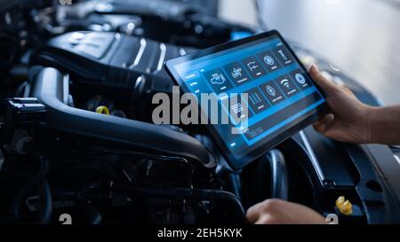 Car Service Manager or Mechanic Uses a Tablet Computer with a Futuristic Interactive Diagnostics Software. Specialist Inspecting the Vehicle in Order Stock Photo