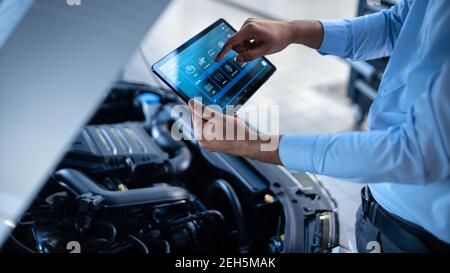 Car Service Manager or Mechanic Uses a Tablet Computer with a Futuristic Interactive Diagnostics Software. Specialist Inspecting the Vehicle in Order Stock Photo