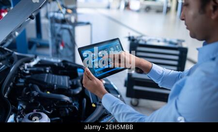 Car Service Manager or Mechanic Uses a Tablet Computer with a Futuristic Interactive Diagnostics Software. Specialist Inspecting the Vehicle in Order Stock Photo