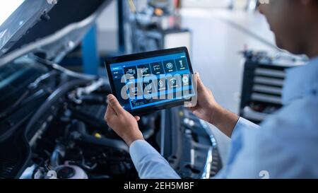 Car Service Manager or Mechanic Uses a Tablet Computer with a Futuristic Interactive Diagnostics Software. Specialist Inspecting the Vehicle in Order Stock Photo