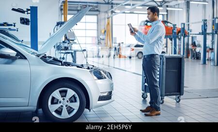 Car Service Manager Uses a Tablet Computer with an Augmented Reality Diagnostics Software. Specialist Inspecting the Car in Order to Find Broken Stock Photo