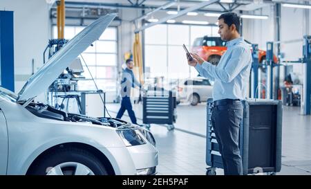 Car Service Manager Uses a Tablet Computer with an Augmented Reality Diagnostics Software. Specialist Inspecting the Car in Order to Find Broken Stock Photo