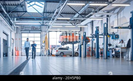 Female Mechanic Checks Diagnostics Results on a Tablet Computer and Explains a Vehicle Breakdown to a Manager. Car Service Employees Talk while Stock Photo