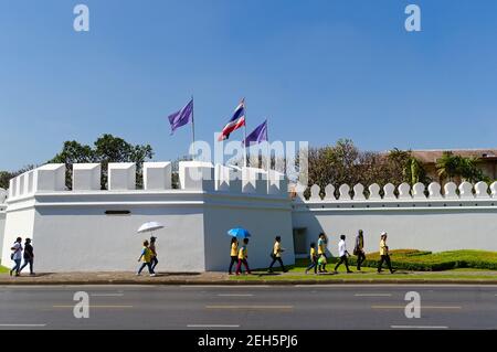 Bangkok, Thailand - December, 2015: People walking along white fortification wall of Grand Palace also know as residence of Kings of Siam. Thai flags Stock Photo