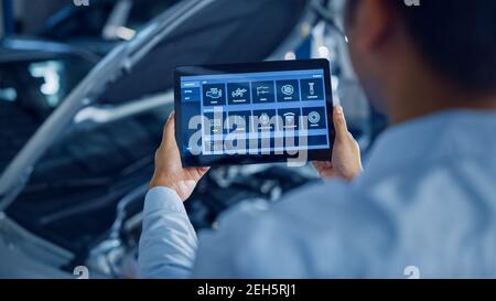 Car Service Manager or Mechanic Uses a Tablet Computer with a Futuristic Interactive Diagnostics Software. Specialist Inspecting the Vehicle in Order Stock Photo