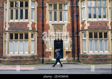 Eton, Windsor, Berkshire, UK. 19th February, 2021. A man walks his dog past the Eton College Hawtrey House. On Monday next week, Prime Minister Boris Johnson is due to announce the plans for pupils to return to schools in England. The earliest likely date is expected to be from 8th March 2021. The famous public boarding school closed early in December last year due to an oubreak of Covid-19 amongst some staff and pupils. Eton College boys come to Eton from around the world so although some pupils may return when the school reopens, others may have to temporarily continue with online learning d