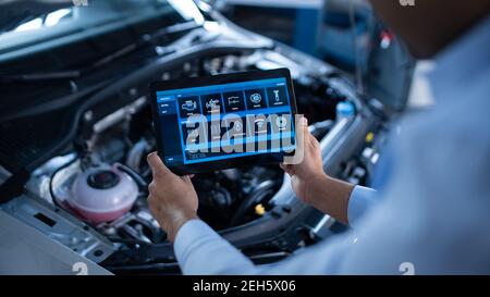 Car Service Manager or Mechanic Uses a Tablet Computer with a Futuristic Interactive Diagnostics Software. Specialist Inspecting the Vehicle in Order Stock Photo