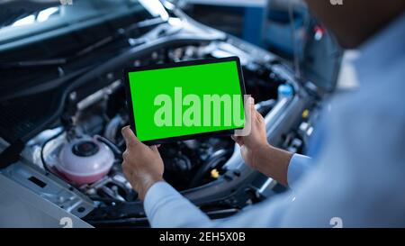 Car Service Manager or Mechanic Uses a Tablet Computer with a Green Screen Mock Up that is Pointed at an Enginer Bay. Specialist Inspecting the Stock Photo