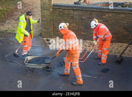 BUCKINGHAM, UK - December 14, 2020. Road workers wearing high visibility hi vis orange clothing, repairing potholes in a street Stock Photo