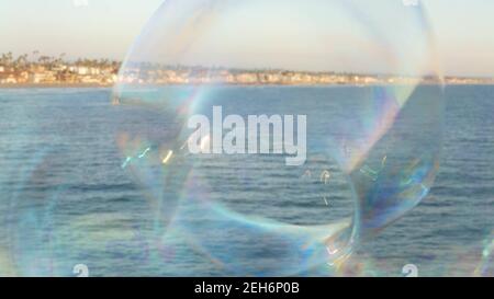 Blowing soap bubbles on ocean pier in California, blurred summertime background. Creative romantic metaphor, concept of dreaming happiness and magic. Stock Photo