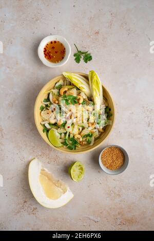 Top down view of a delicious vegan Bali style pomelo salad with chicory, cucumber, cashews, coriander , toasted coconut and chill lime dressing Stock Photo