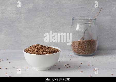 Raw buckwheat in a white ceramic bowl on a light gray textured background, horizontal Stock Photo