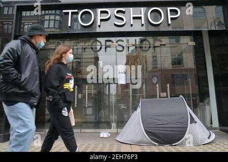 London, UK. 19th Feb, 2021. A couple wearing face masks as a precaution against the spread of covid-19 walking past a rough sleeper's tent in front of a closed down Topshop in Central London. Covid-19 cases continue to drop in the UK, as the government continues to fight the spread of the virus as lockdown stays in Central London. Credit: SOPA Images Limited/Alamy Live News Stock Photo