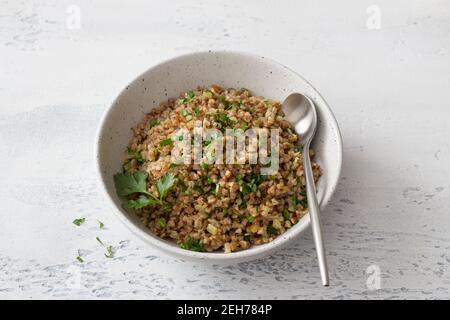 A bowl of vegan buckwheat porridge with herbs and onions on a light gray background. Natural healthy food Stock Photo
