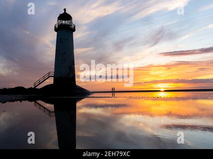 Lighthouse standing in pool of water stunning sunset sunrise reflection reflected in water and sea steps up building north Wales seashore sand beach Stock Photo