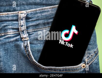 Tik Tok logo on black screen of smartphone in jeans pocket on a green background Stock Photo