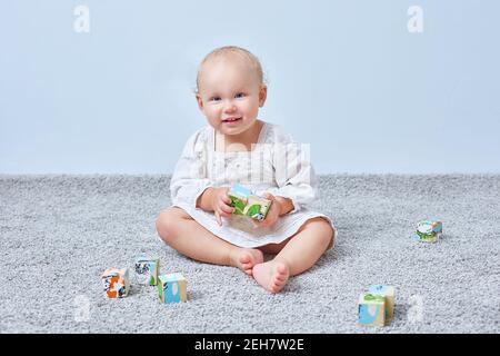 Funny girl playing wooden cubes on the carpet. Copy space. Stock Photo