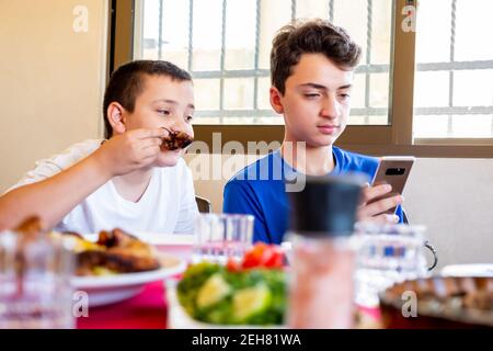 Arabic Muslim boys using their smartphones while eating and taking photos of the food Stock Photo