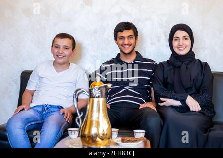 Happy Arabic family sitting together enjoying Arabic coffee and sweets and talking to each other Stock Photo