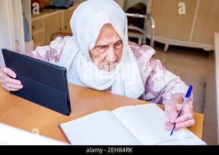 Old woman portrait studying ,writing and learning using tablet and notebook Stock Photo