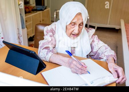 Old woman portrait studying ,writing and learning using tablet and notebook Stock Photo