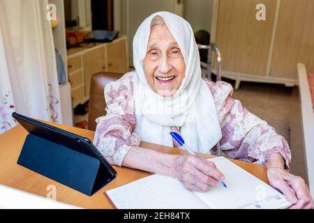 Old woman portrait studying ,writing and learning using tablet and notebook Stock Photo