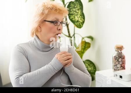 Elderly woman using asthma machine on light background Stock Photo