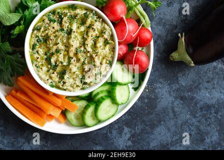 Close up view of baba ganoush (roasted eggplant dip) in bowl and fresh organic vegetables over blue stone background with free text space. Vegetarian Stock Photo