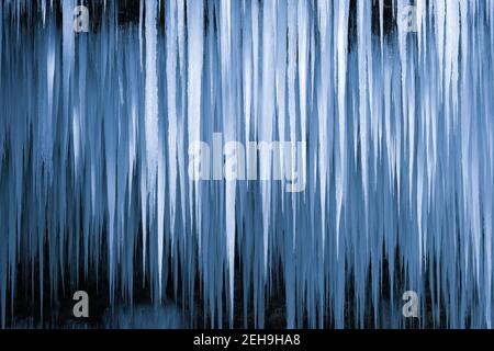 Beautiful long icicles of a frozen waterfall. Water flowing and crashing down and ice dripping down in a cold eery and dark mountain cave Stock Photo