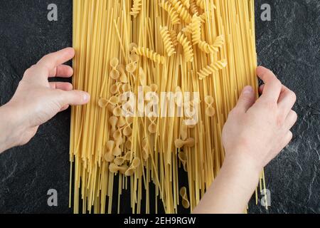 Woman hands touching various pasta on dark surface Stock Photo