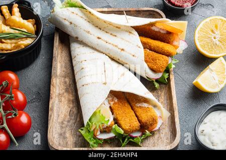Tortilla roll with fish fingers, cheese and vegetables set, on wooden tray, on gray background Stock Photo