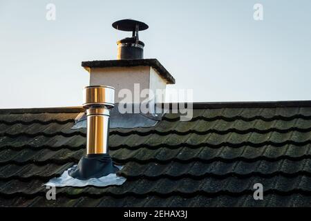 Modern metal wood burning stove chimney on a grey slate roof with the original chimney Stock Photo