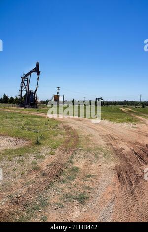 Oil rigs and old metal tanks out in field with muddy tracks leading out to them - vertical Stock Photo