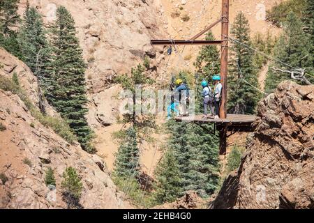 People on a platform in the mountains getting ready to rappel down - man helping woman in harness as she gets ready to go while others look on Stock Photo