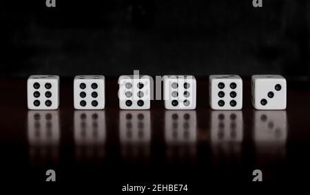 Six dice on a table with reflection and black background, five dice showing six, one dice showing three Stock Photo