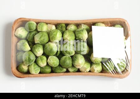 The heads of Brussels sprouts are randomly placed in a cardboard box and covered with transparent foil. The box is on a white table. Closeup. View fro Stock Photo