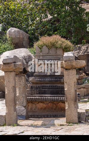 Anegundi, Karnataka, India - November 9, 2013: Navabrindavana island and temple. Closeup of ruinous brown stone monument with green foliage screen in Stock Photo