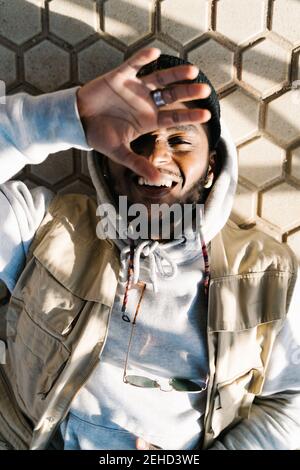 Top view of calm young bearded African American male in trendy outfit lying on ground with closed eyes on sunny day Stock Photo