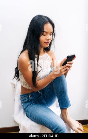 Long hair Asian Woman sitting at home using a mobile phone Stock Photo