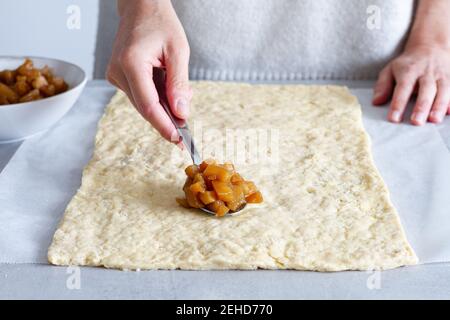 Crop anonymous female cook putting soft cooked apple slices on dough while preparing pastry at home Stock Photo