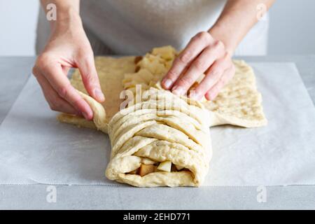 Crop unrecognizable female chef preparing delicious apple pastry with soft braided dough and fruit slices in house Stock Photo
