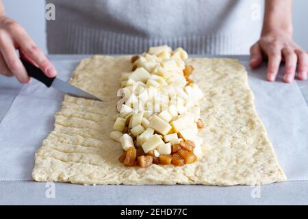 Crop anonymous female cook cutting raw dough with delicious fresh and cooked apple slices while preparing braided pastry on baking paper Stock Photo