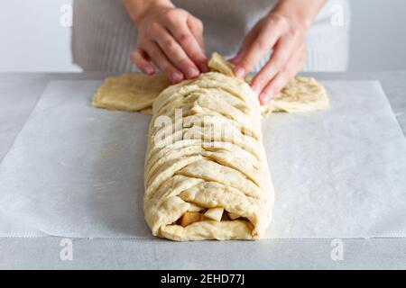 Crop unrecognizable female chef preparing delicious apple pastry with soft braided dough and fruit slices in house Stock Photo