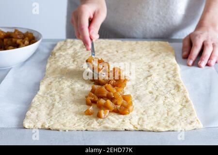 Crop anonymous female cook putting soft cooked apple slices on dough while preparing pastry at home Stock Photo