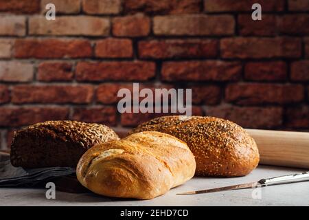 White and rye bread with cereals and appetizing crust on cutting board against brick wall in bakehouse Stock Photo